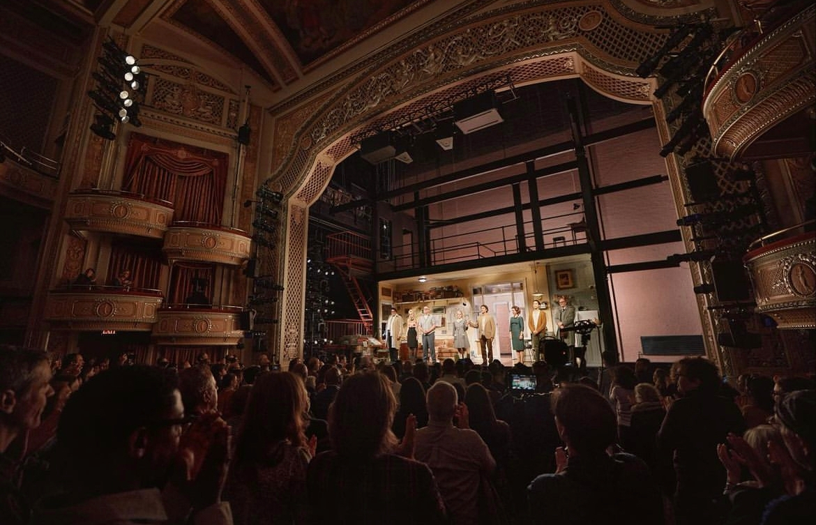 The Sign in Sidney Brustein’s Window cast on the apartment set, viewed from the audience within the ornate theatre.